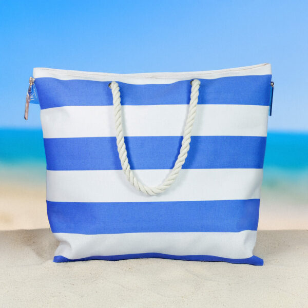 Blau-weiß gestreifte Inis Strandtasche mit Kordelgriffen auf hellem Sand vor dem Meer