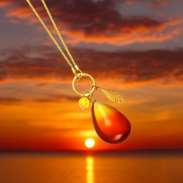 Vergoldete Silber Halskette mit cognacfarbenem Bernstein und Blattanhänger vor Sonnenuntergang am Meer